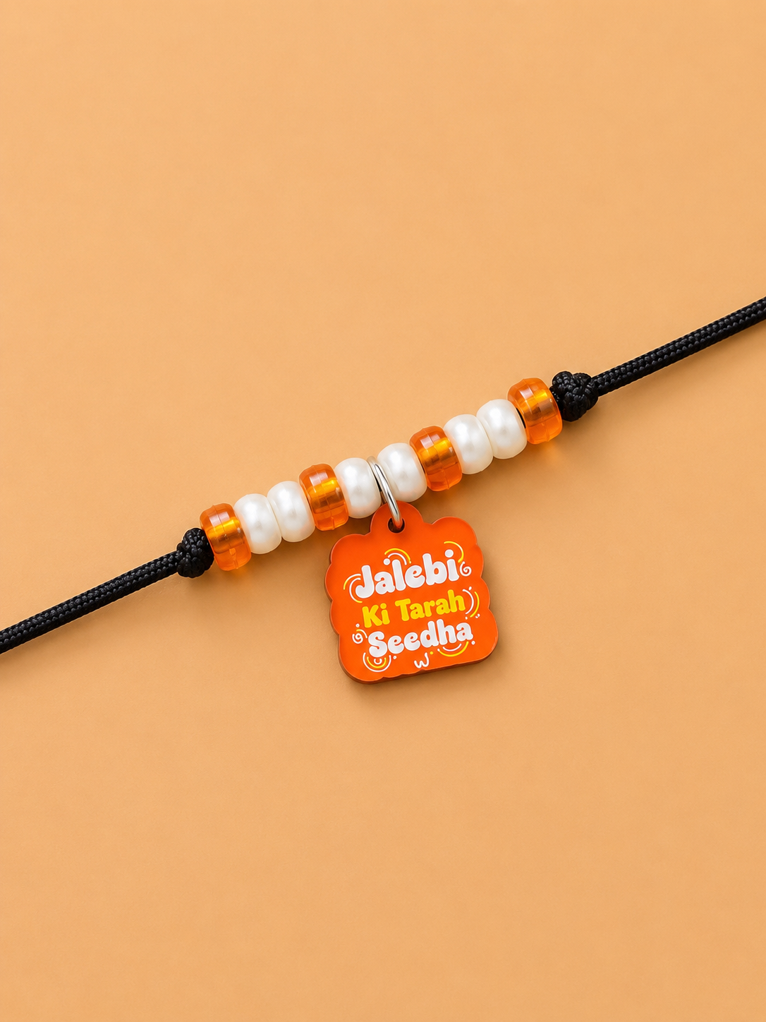 A beaded dog paw rakhi featuring white and orange beads with a small orange tag that reads 'Jalebi Ki Tarah Seedha' 