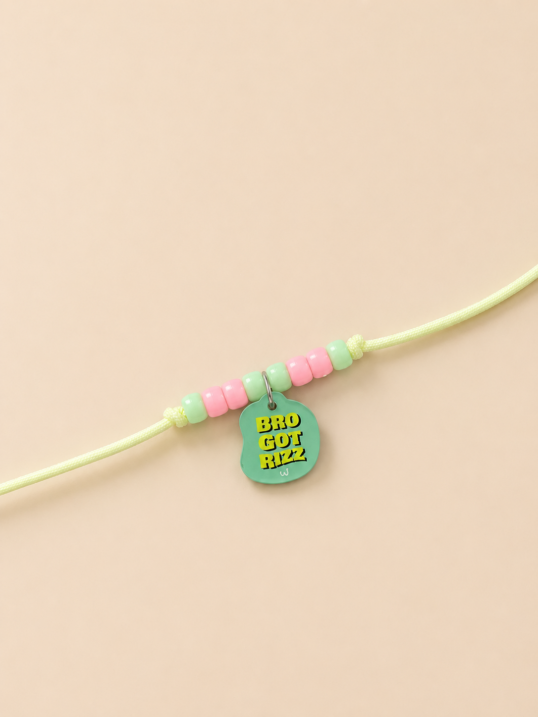 A light green rakhi for dogs and cats featuring pastel pink and mint green beads, with a mint green guitar-shaped charm displaying the text 'BRO GOT RIZZ' in yellow.